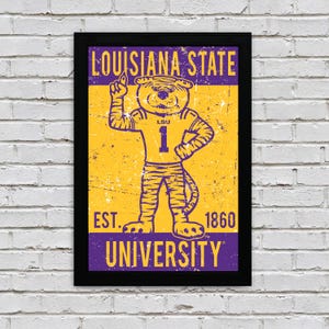 May include: Framed poster featuring the Louisiana State University mascot, a tiger wearing a purple jersey with the number 1. The poster has a distressed, vintage look with the words "LOUISIANA STATE UNIVERSITY" and "EST. 1860". The colour scheme is purple and gold.