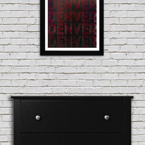 May include: A framed print with the word "DENVER" repeated five times in a red, white, and blue color scheme. The background is black with a subtle galaxy-like pattern.