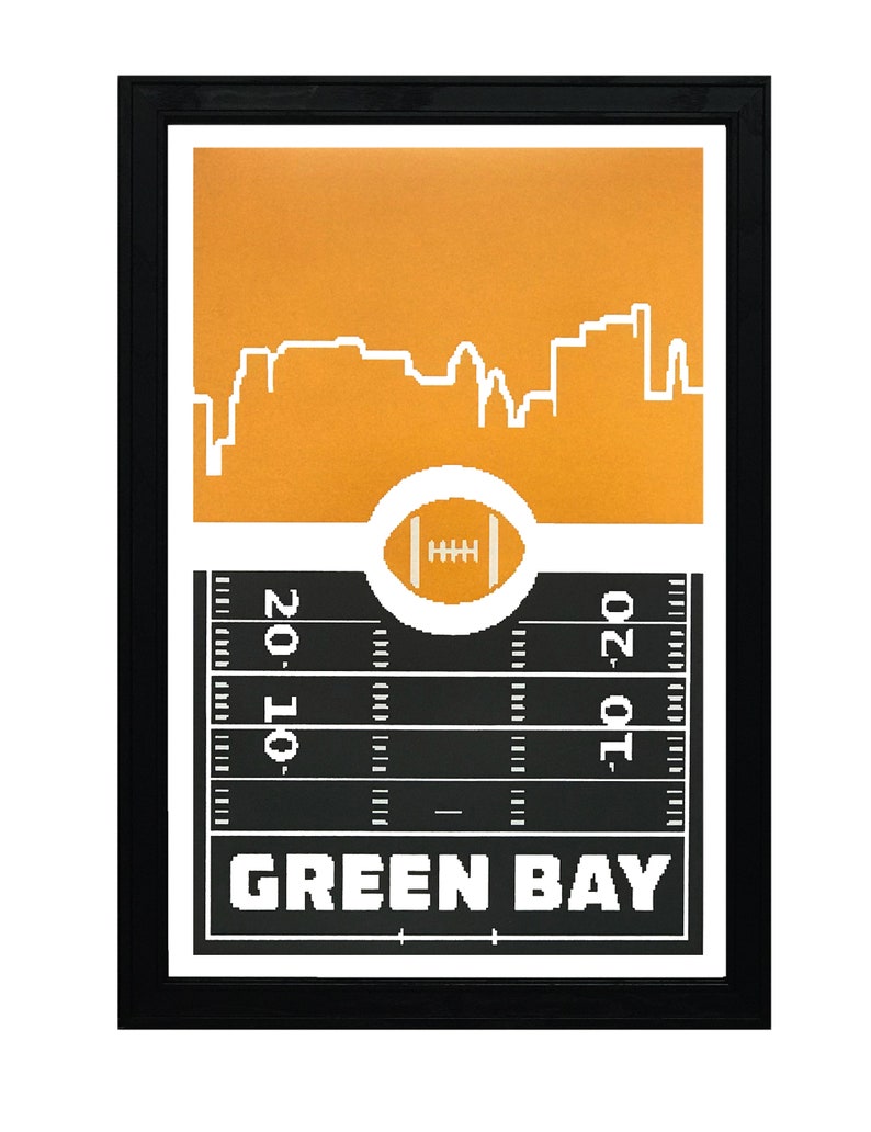 May include: A framed print with a black frame and a gold background. The print features a white silhouette of the Green Bay skyline with a football field and a football in the center. The text "GREEN BAY" is printed in white at the bottom of the print.