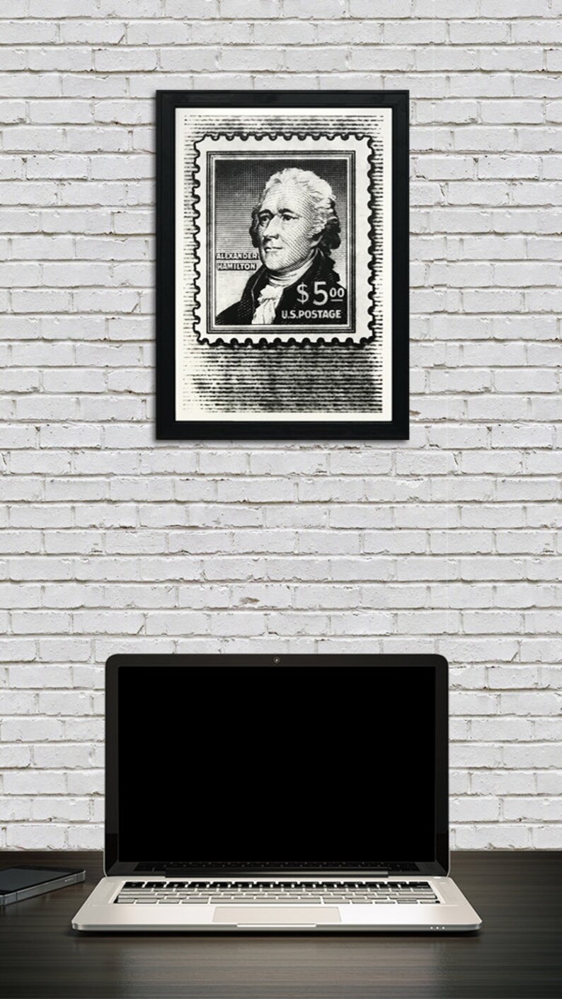 May include: Black and white framed print of a vintage postage stamp featuring a portrait of Alexander Hamilton with the text "Alexander Hamilton $5.00 U.S. Postage".