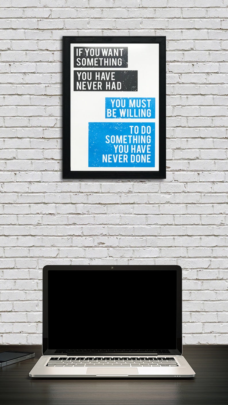 May include: A motivational quote in a black frame on a white brick wall. The quote reads: "If you want something you have never had, you must be willing to do something you have never done."