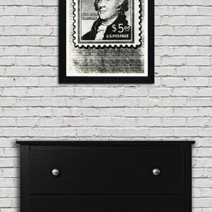 May include: Black and white framed print of a vintage postage stamp featuring a portrait of Alexander Hamilton with the text "ALEXANDER HAMILTON $5.00 U.S. POSTAGE".