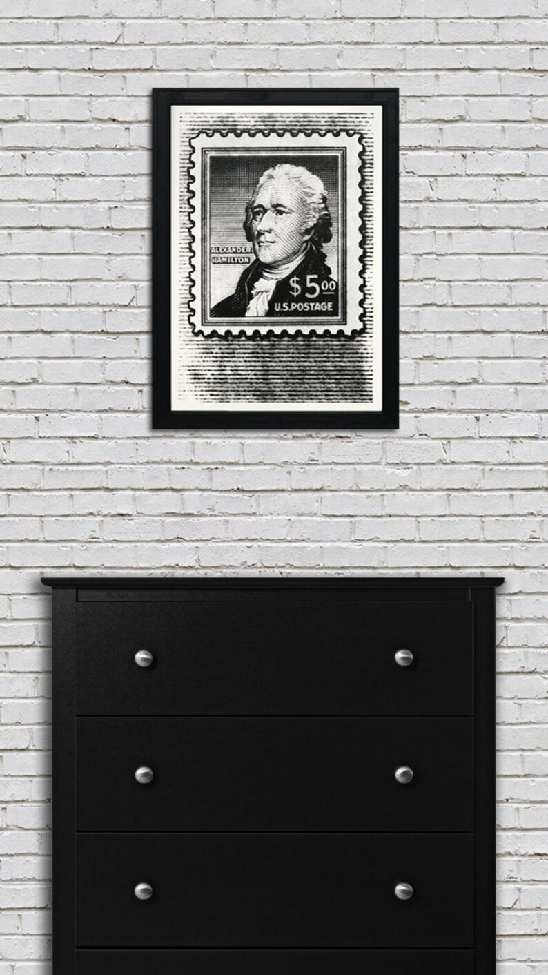May include: Black and white framed print of a vintage postage stamp featuring a portrait of Alexander Hamilton with the text "ALEXANDER HAMILTON $5.00 U.S. POSTAGE".