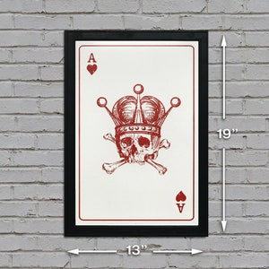 May include: Framed art print of an Ace of Hearts playing card, featuring a skull wearing a crown and crossed bones. The print is 19 inches tall and 13 inches wide, with a black frame and red ink design on a white background.