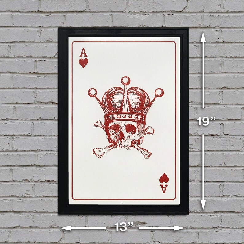 May include: Framed art print of an Ace of Hearts playing card, featuring a skull wearing a crown and crossed bones. The print is 19 inches tall and 13 inches wide, with a black frame and red ink design on a white background.