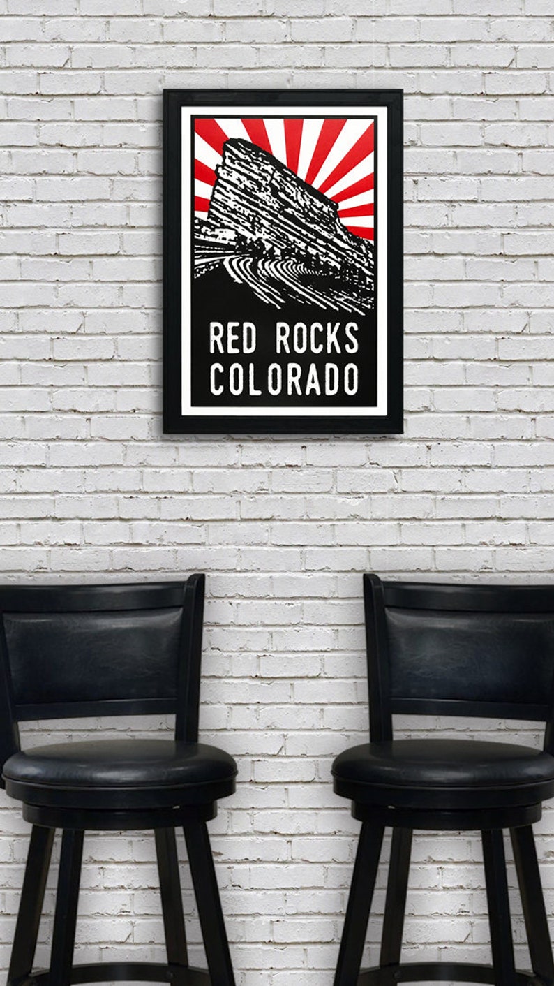 May include: A black framed poster with a red and white sunburst design behind a black and white illustration of Red Rocks Amphitheatre in Colorado. The text "RED ROCKS COLORADO" is printed in white below the illustration.