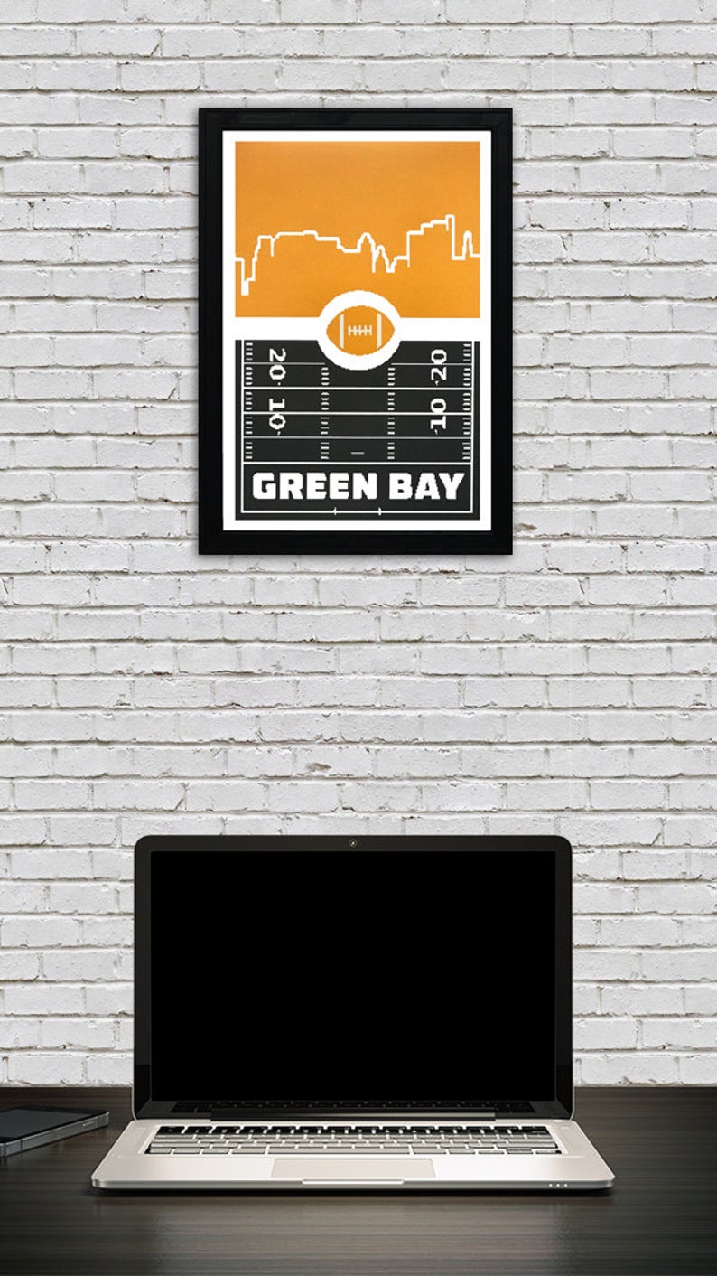 May include: A black framed print with a yellow background and a white silhouette of the Green Bay skyline. The print features a football field with the words "Green Bay" at the bottom.