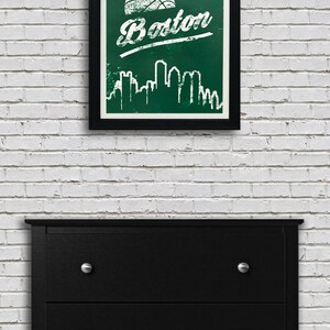 May include: A framed print with a green background and white text that says "Boston". A basketball is above the text and a white silhouette of the Boston skyline is below the text.