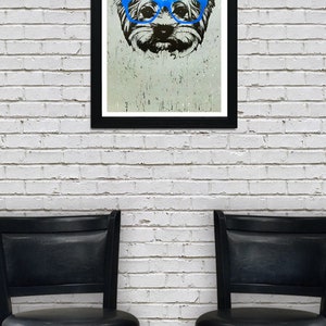 May include: A black framed print of a dog wearing blue glasses. The dog is a Yorkshire Terrier and the print is on a white brick wall background. Two black bar stools are in the foreground.