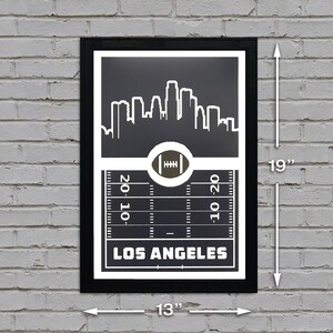 May include: Black and white print of the Los Angeles skyline with a football field and football in the center. The print is framed in black and measures 13 inches by 19 inches.
