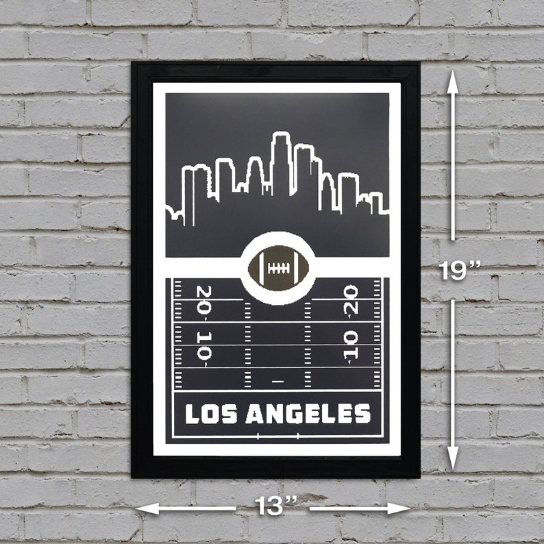 May include: Black and white print of the Los Angeles skyline with a football field and football in the center. The print is framed in black and measures 13 inches by 19 inches.