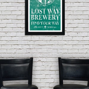 May include: A framed poster with a distressed green background and a white compass design. The text reads "Lost Way Brewery Find Your Way" with the location "Holdrege, Nebraska" below.