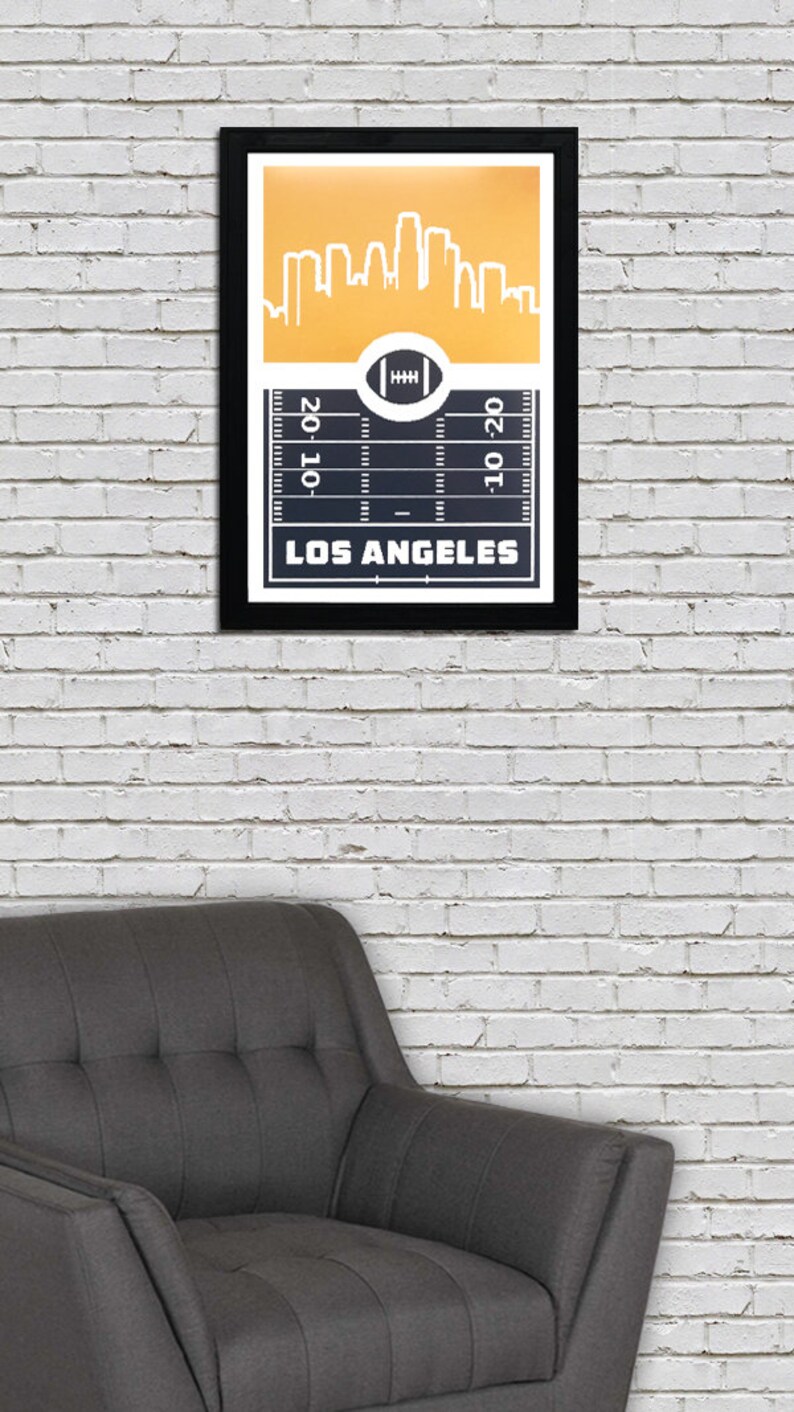 May include: A framed print with a gold background and a black and white silhouette of the Los Angeles skyline. The bottom of the print features a black and white football field with the words "Los Angeles" and "20-10-20".