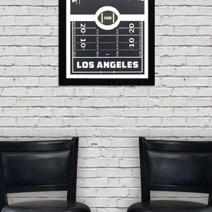 May include: Black and white framed print of a football field with a skyline of Los Angeles, California. The text "LOS ANGELES" is printed below the field.
