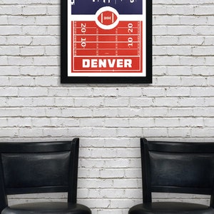 May include: A framed print with a red and white football field design and a blue skyline of Denver, Colorado. The text "DENVER" is printed in white at the bottom of the print.
