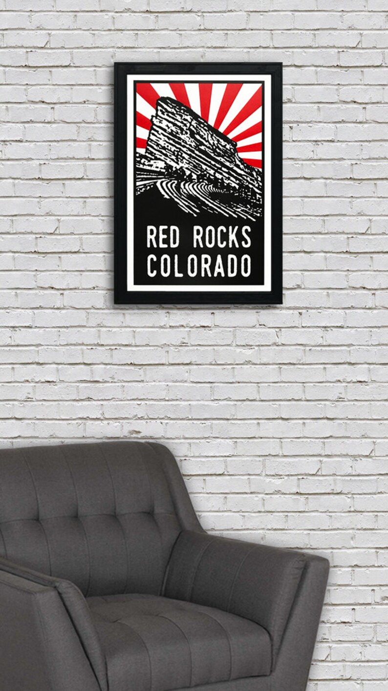 May include: A black and white poster with a red sunburst design. The poster features a silhouette of Red Rocks Amphitheatre in Morrison, Colorado. The text "RED ROCKS COLORADO" is printed in white at the bottom of the poster.