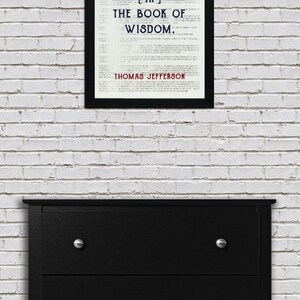 May include: A framed print with the quote "HONESTY IS THE FIRST CHAPTER [IN] THE BOOK OF WISDOM. THOMAS JEFFERSON" displayed above a black dresser with silver knobs. The print is in a black frame and is against a white brick wall.