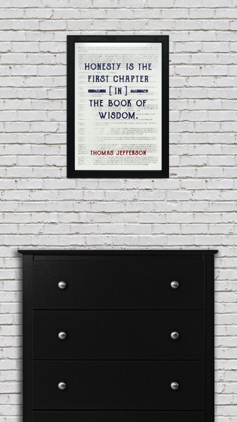 May include: A framed print with the quote "HONESTY IS THE FIRST CHAPTER [IN] THE BOOK OF WISDOM. THOMAS JEFFERSON" displayed above a black dresser with silver knobs. The print is in a black frame and is against a white brick wall.