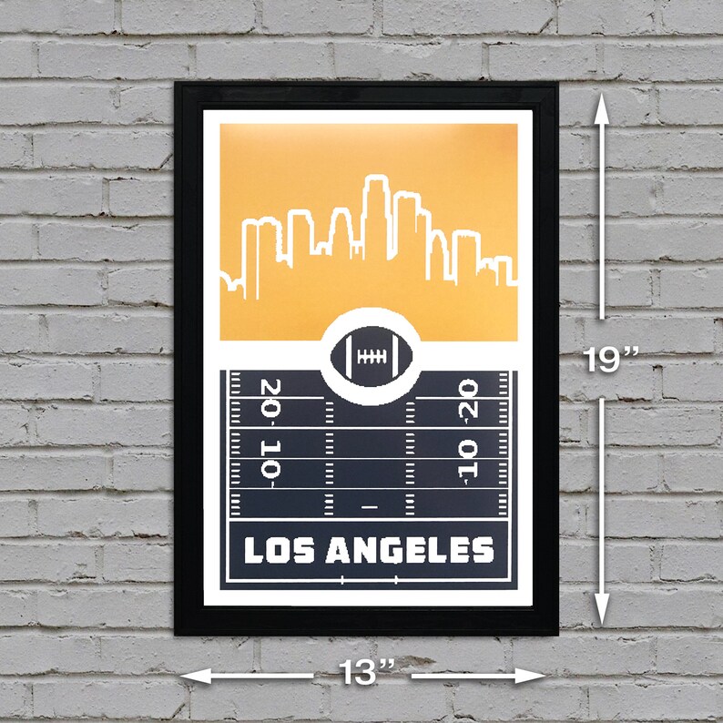 May include: A black framed poster with a gold background featuring a white silhouette of the Los Angeles skyline. The bottom of the poster shows a black and white football field with the text "LOS ANGELES" in white.