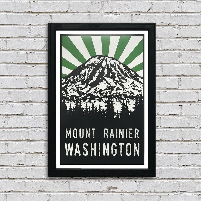 May include: A black framed poster with a vintage style illustration of Mount Rainier in Washington state. The mountain is depicted in black and white with a green sunburst behind it. The text "MOUNT RAINIER WASHINGTON" is printed in white at the bottom of the poster.