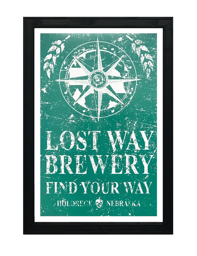 May include: A vintage-style sign with a distressed green background and white text. The sign features a compass with a white star in the center and the words "Lost Way Brewery Find Your Way Holdrege Nebraska".