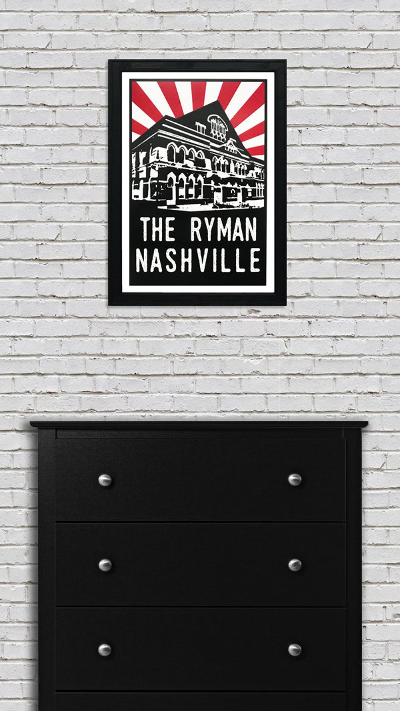 May include: Black and white illustration of The Ryman Auditorium in Nashville, Tennessee. The building is depicted with a red and white sunburst behind it. The text "The Ryman Nashville" is printed below the building.