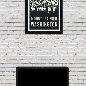 May include: A black and white illustration of Mount Rainier, a mountain in Washington state, with green rays emanating from the peak. The text "MOUNT RAINIER WASHINGTON" is below the mountain.