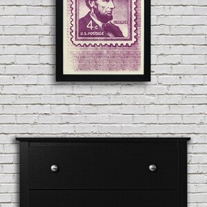 May include: A framed print of a vintage US postage stamp featuring a portrait of Abraham Lincoln. The stamp is purple and reads "4&cent; U.S. POSTAGE" and "LINCOLN".