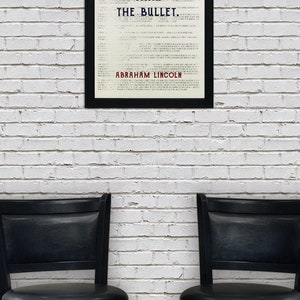 May include: A framed print with a white background and black text that reads "The ballot is stronger than the bullet. Abraham Lincoln". The print is hanging on a white brick wall. Two black bar stools are in front of the print.