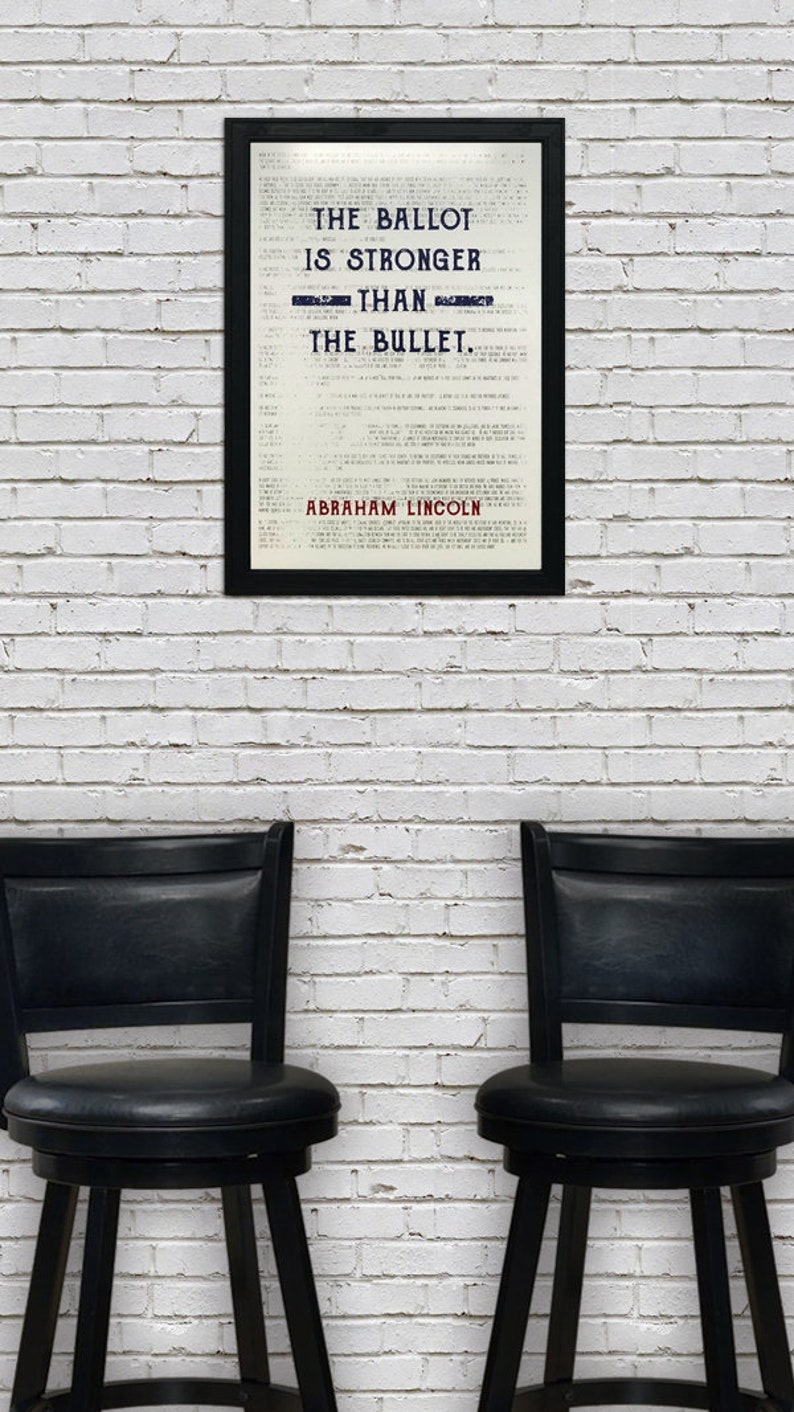 May include: A framed print with a white background and black text that reads "The ballot is stronger than the bullet. Abraham Lincoln". The print is hanging on a white brick wall. Two black bar stools are in front of the print.