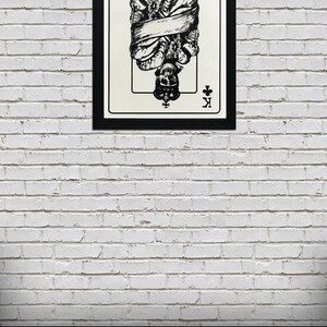 May include: A black and white illustration of the King of Clubs playing card. The King is depicted as a skeleton wearing a crown and holding a scepter. The card is framed in black and hanging on a white brick wall. A pile of poker chips is in the foreground.