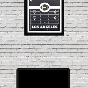 May include: Black and white print of the Los Angeles skyline with a football field graphic and the text "Los Angeles" at the bottom.