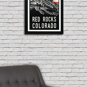K&ouml;nnte beinhalten: Eine Schwarzwei&szlig;illustration des Red Rocks Amphitheaters in Morrison, Colorado. Die Illustration zeigt ein rotes und wei&szlig;es Sonnenstrahlen-Design hinter der Felsformation. Der Text "RED ROCKS COLORADO" ist unter der Illustration gedruckt.