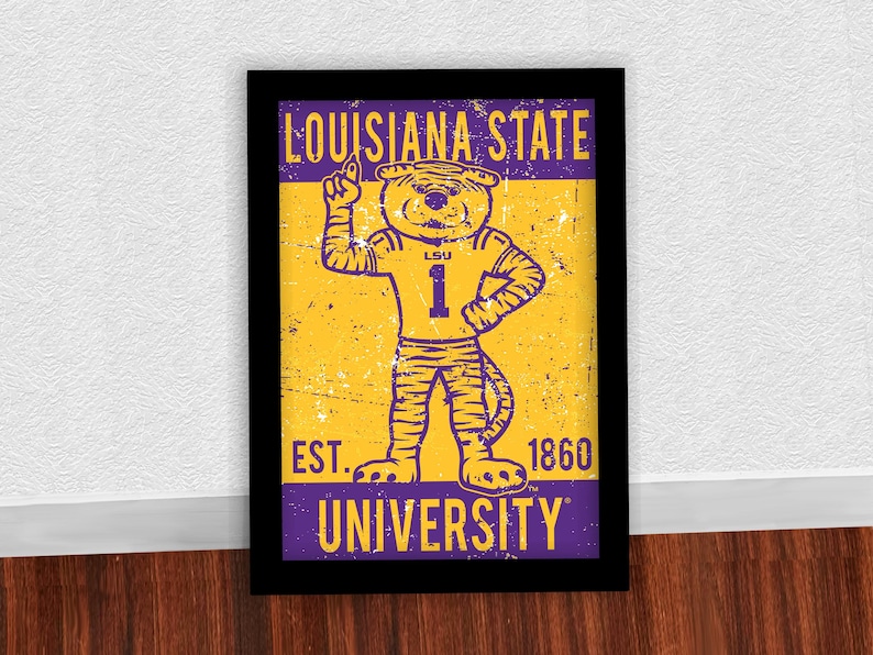 May include: Framed print featuring the Louisiana State University mascot, a tiger wearing a jersey with the number 1. The print has a distressed, vintage look with the words "Louisiana State University" and "Est. 1860". The colour scheme is gold, purple, and black.