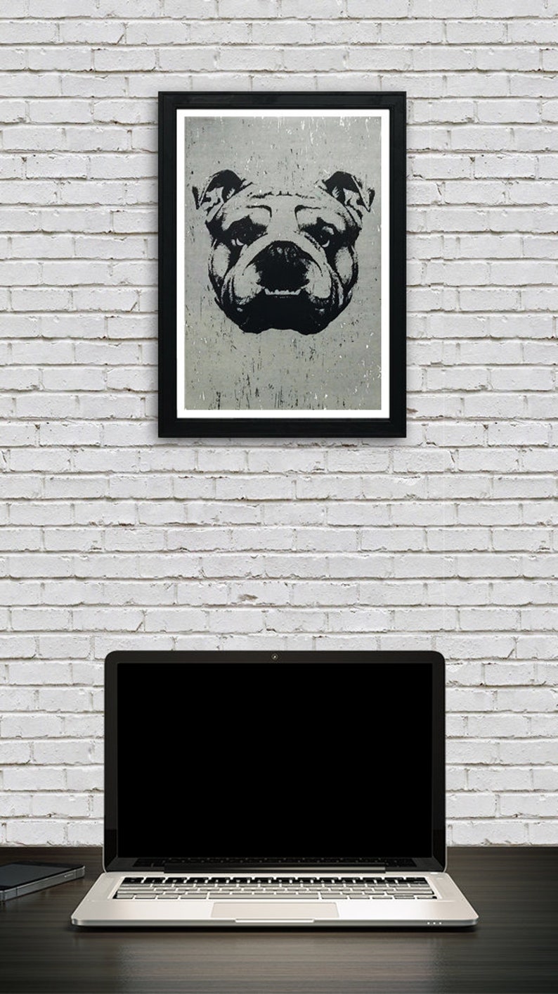 Puede incluir: Una ilustraci&oacute;n en blanco y negro de la cara de un bulldog en un marco negro colgado en una pared de ladrillo blanco sobre un ordenador port&aacute;til.