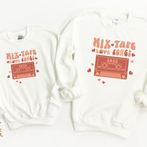 May include: Two white sweatshirts with a retro cassette tape graphic and the text "Mix-Tape Love Songs" in pink and orange. The text "XOXO" is on the cassette tape.