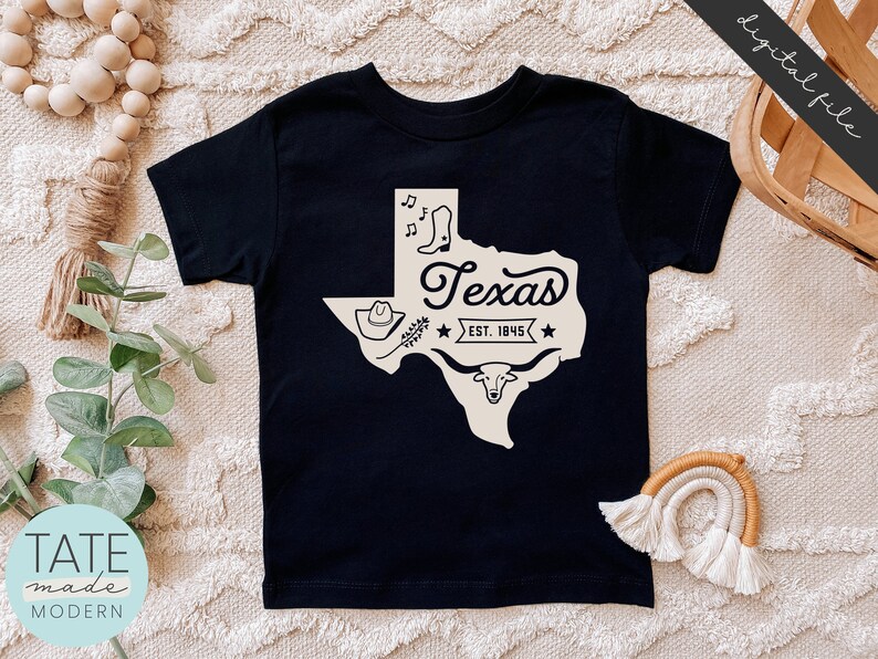 May include: Black t-shirt with a white outline of the state of Texas, a cowboy hat, boots, and a longhorn steer. The text "Texas Est. 1845" is inside the state outline.
