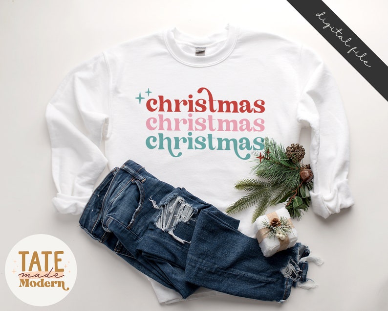 Pode incluir: Camisola branca de manga comprida com o texto "christmas christmas christmas" em vermelho, rosa e azul.