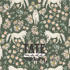 Op de afbeelding: Een naadloos patroon met witte eenhoorns en roze en gele bloemen op een donkergroene achtergrond. De tekst "TATE made Modern" is gecentreerd op het patroon.