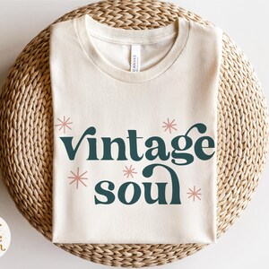 May include: A beige t-shirt with the text "vintage soul" in dark green letters with pink stars around the text.