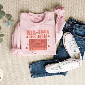 May include: Pink sweatshirt with a graphic of a cassette tape and the text "Mix Tape Love Songs" with hearts around the text.