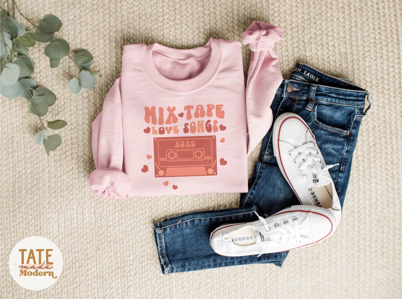 May include: Pink sweatshirt with a graphic of a cassette tape and the text "Mix Tape Love Songs" with hearts around the text.