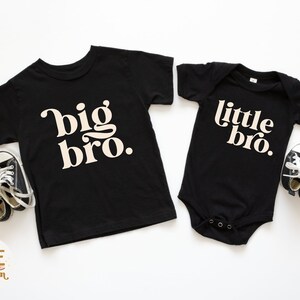 Puede incluir: Dos camisetas negras con texto blanco. La camiseta m&aacute;s grande dice "big bro." La camiseta m&aacute;s peque&ntilde;a dice "little bro."