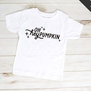 May include: White t-shirt with black text that reads "Oh hey pumpkin" with plus signs around the text.