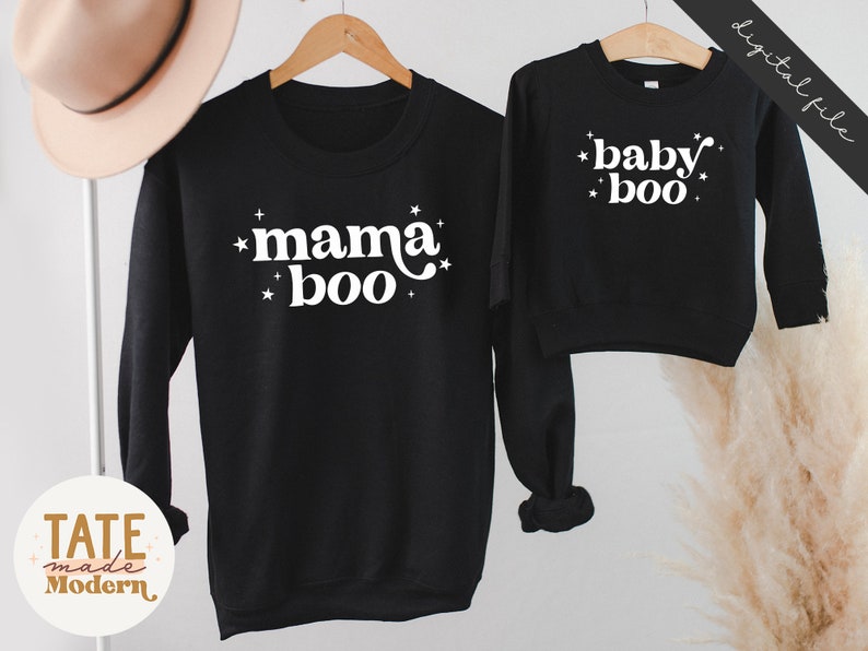 May include: Two black sweatshirts with white text. The larger sweatshirt says "mama boo" with stars around the text. The smaller sweatshirt says "baby boo" with stars around the text.