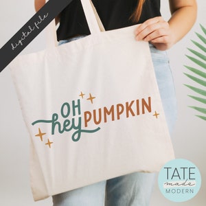 May include: A white tote bag with the text "Oh hey pumpkin" in teal and orange lettering with gold stars. The text is in a handwritten style font.