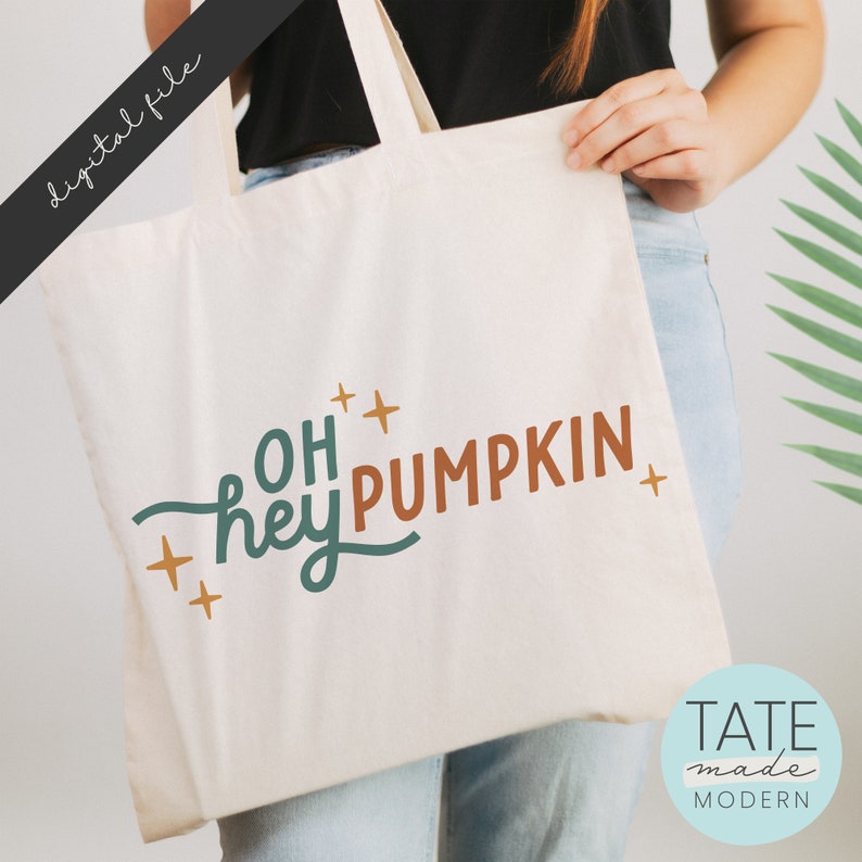 May include: A white tote bag with the text "Oh hey pumpkin" in teal and orange lettering with gold stars. The text is in a handwritten style font.