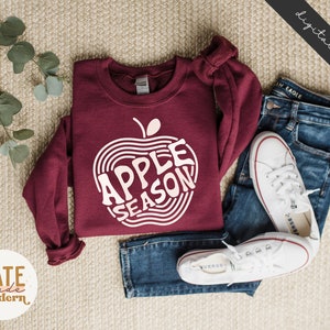 May include: A maroon sweatshirt with a white graphic of an apple with the text "Apple Season" inside the apple.