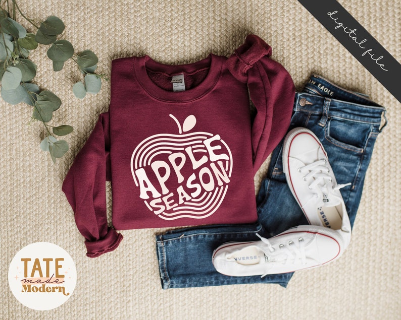 May include: A maroon sweatshirt with a white graphic of an apple with the text "Apple Season" inside the apple.