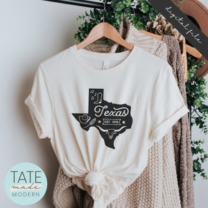 May include: A white t-shirt with a black outline of the state of Texas, with the word "Texas" and "Est. 1945" inside the outline. There are also images of a cowboy hat, boots, and a longhorn steer inside the outline.